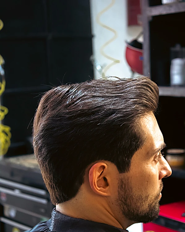 Corte terminado con volumen peinado hacia atrás y barba delineada, visto de tres cuartos