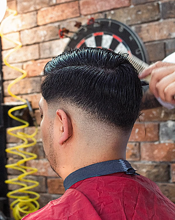 Nuca con desvanecido alto y cabello peinado hacia atrás, con capa roja y una manguera de aire amarilla al fondo