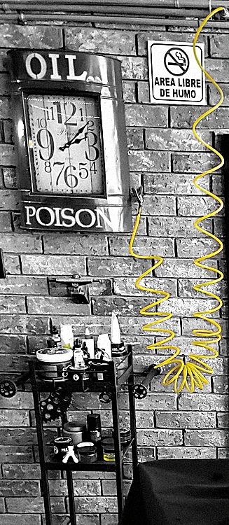 Reloj rojo con letrero Oil Poison sobre la pared de ladrillo, junto a una manguera de aire amarilla en espiral y un carrito de productos